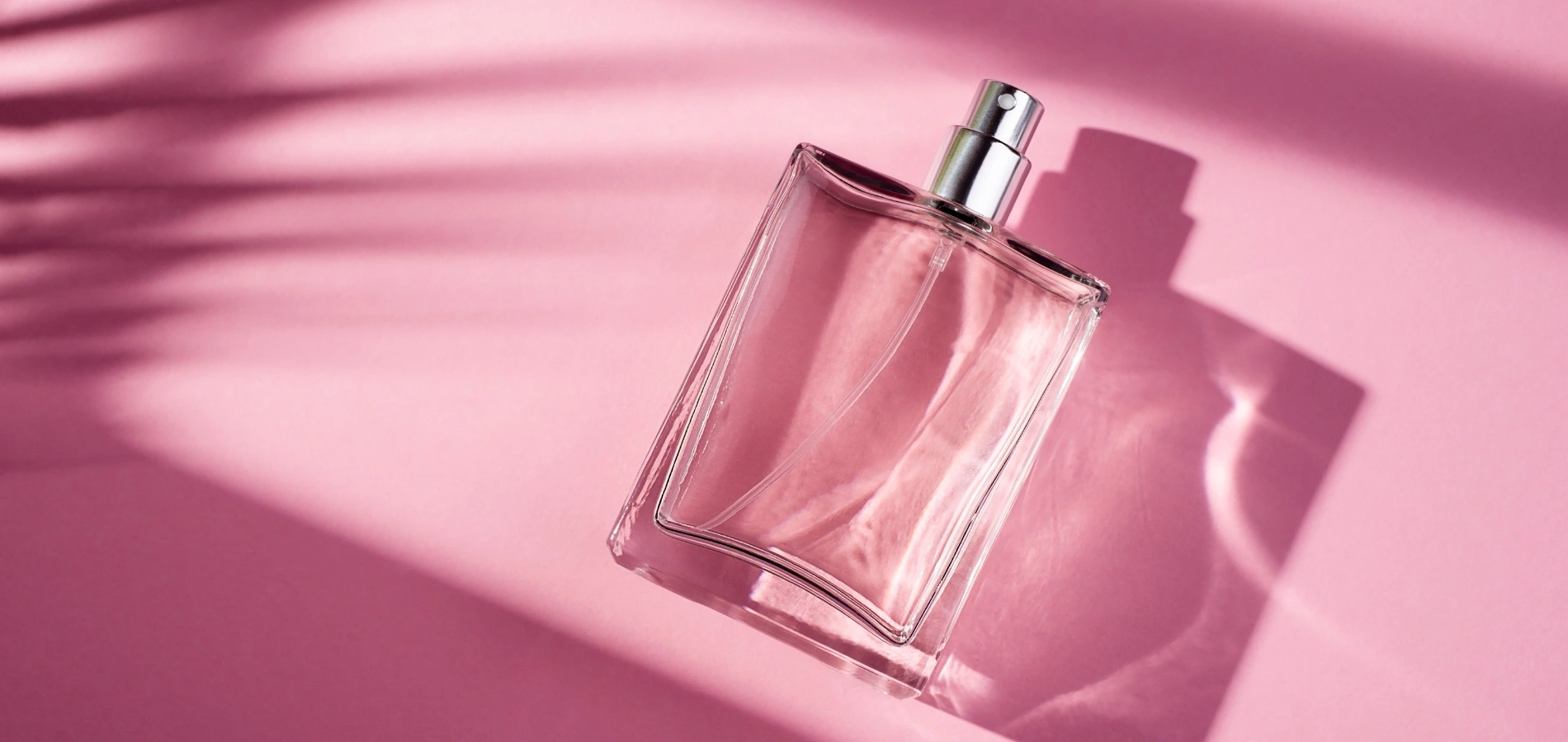 a clear perfume bottle on a pink background